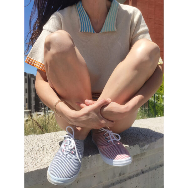 A young woman sitting on a wall, wearing her plain knit t-shirt with colourful accents on the arm, waist and neck bands.