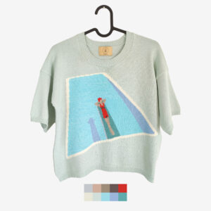 An intarsia knit t-shirt with a woman laying on a springboard at the swimming pool. Featuring the mint, blue, dark blue, red and green colours.