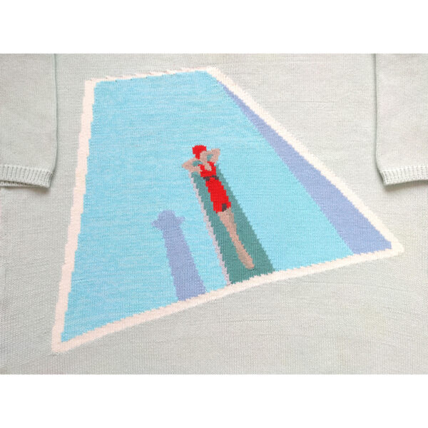 A close up shot of a knit t-shirt with a woman laying on a springboard at the swimming pool.