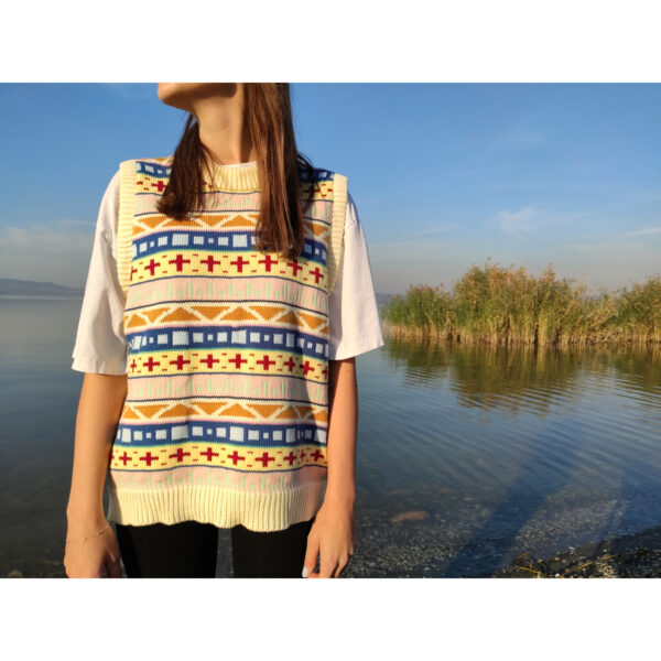A young woman standing by the lake, wearing the Fare Aisle #1 knit vest.