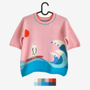 The catalogue shot of a surfing ghost themed pink intarsia knit t-shirt, featuring a ghost surfing on big blue waves.