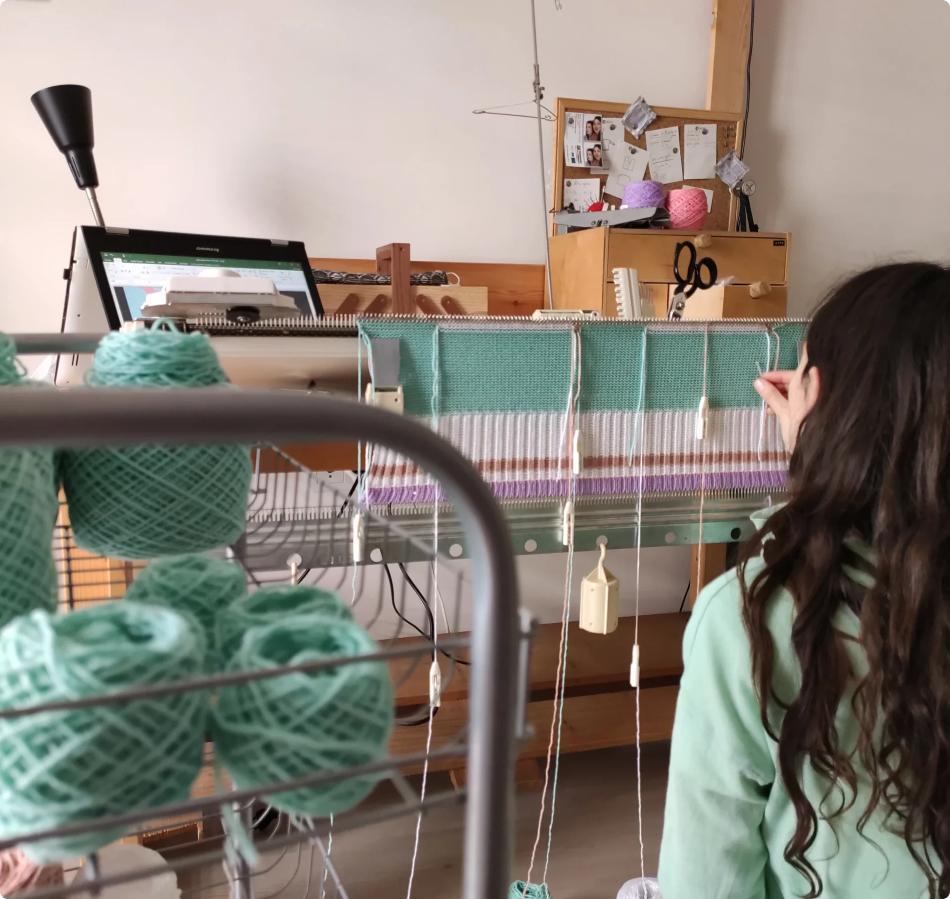 Knitter working on a vintage knitting machine, with mint coloured yarns.