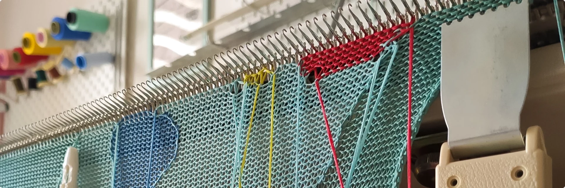 A close up shot of a work in progress on the vintage knitting machine, red, yellow, blue and yellow yarns.