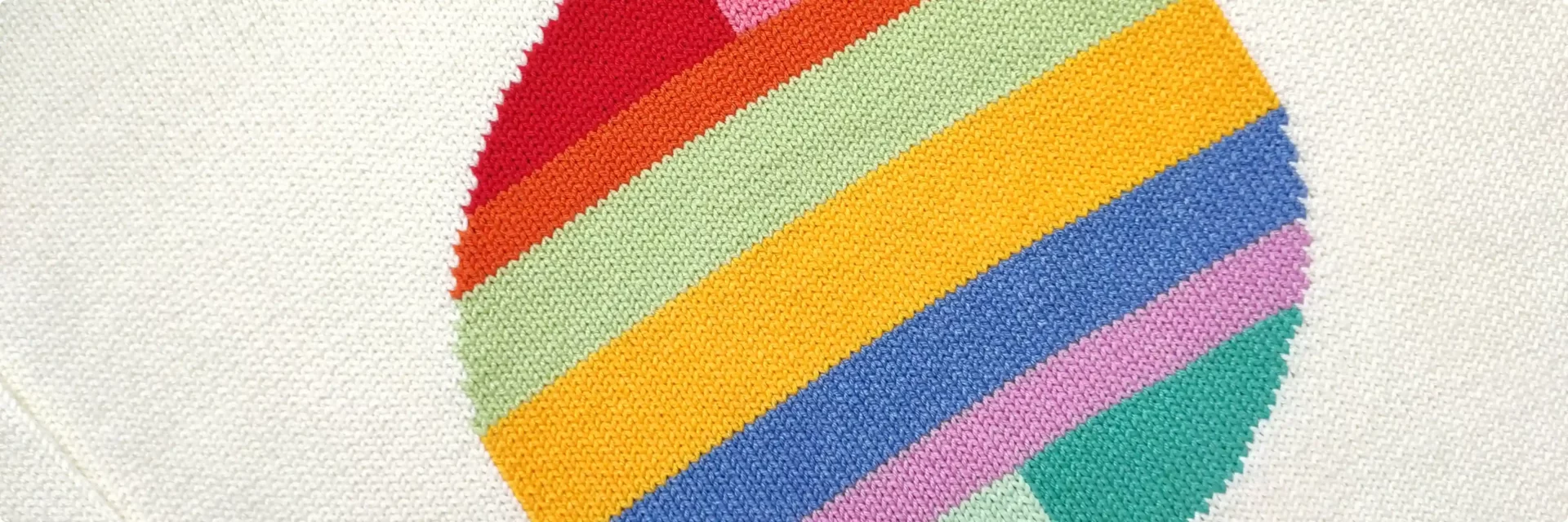 A close up shot of a sweater, displaying a round shape with rainbow colours on the center of the sweater.