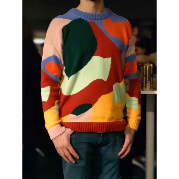 A young man wearing colourful sweater with abstract shapes indoors.