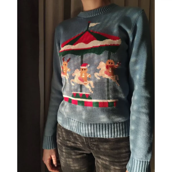 A young women wearing the Christmas sweater Cookie-Go-Round in a dimly lit room, the sweater features three gingerbread men riding an Xmas themed merry-go-round.